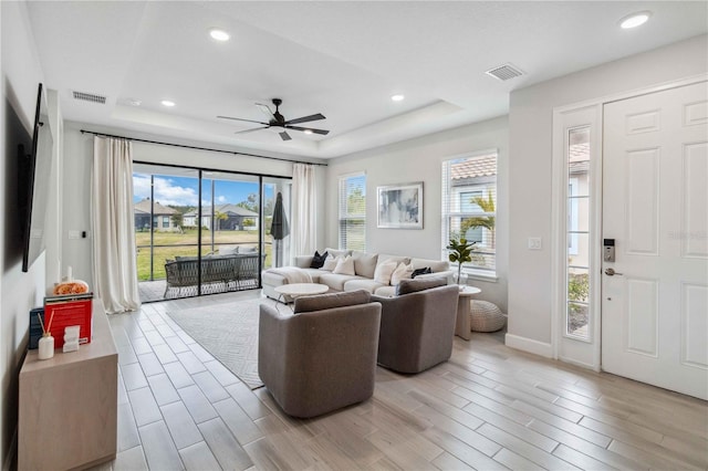 living room with a raised ceiling, ceiling fan, and light hardwood / wood-style floors