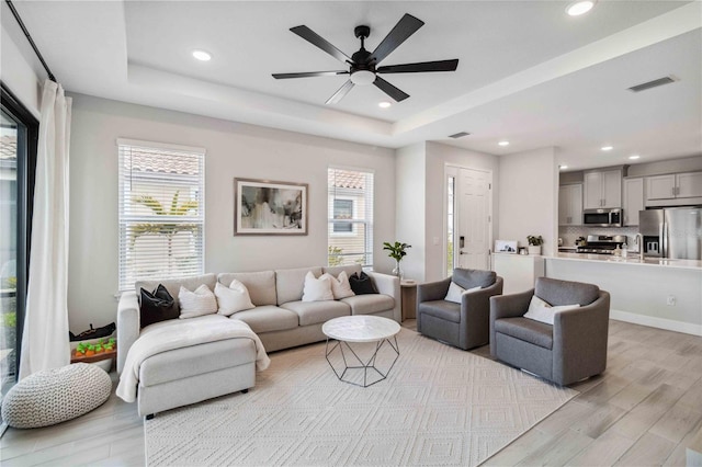 living room featuring a tray ceiling, plenty of natural light, light hardwood / wood-style floors, and ceiling fan