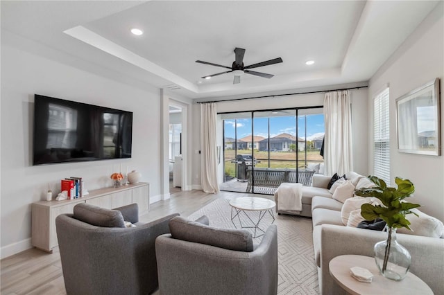 living room with a tray ceiling, light hardwood / wood-style flooring, and ceiling fan