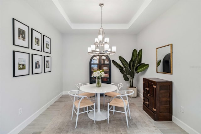 dining space with a tray ceiling, light hardwood / wood-style flooring, and a notable chandelier