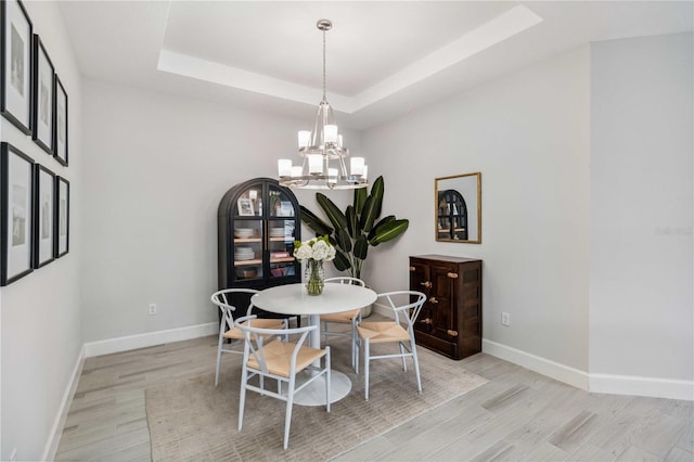 dining area featuring a notable chandelier, light hardwood / wood-style flooring, and a raised ceiling