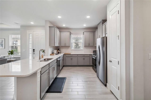 kitchen featuring sink, a breakfast bar, appliances with stainless steel finishes, gray cabinetry, and tasteful backsplash