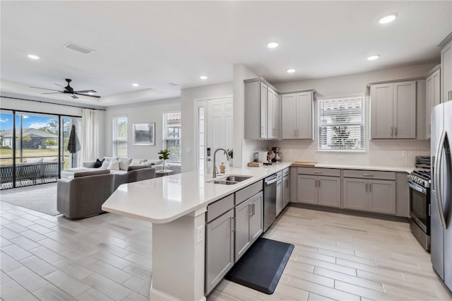 kitchen featuring sink, gray cabinetry, backsplash, stainless steel appliances, and kitchen peninsula