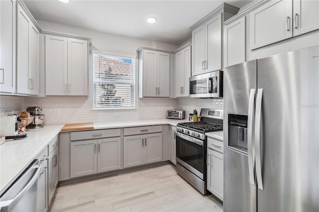 kitchen featuring tasteful backsplash, stainless steel appliances, gray cabinets, and light hardwood / wood-style flooring