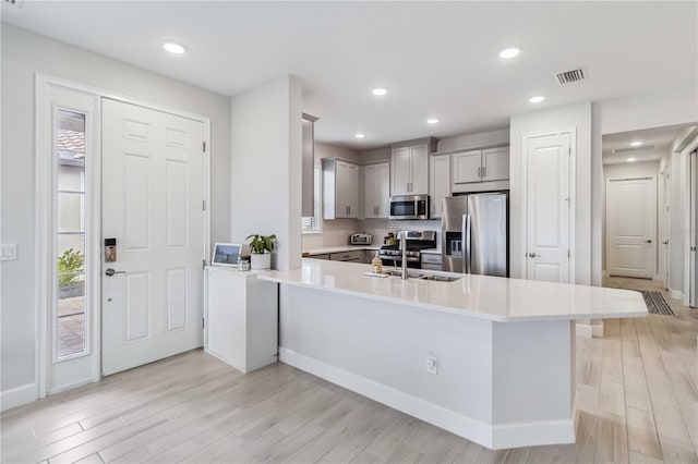 kitchen featuring sink, light hardwood / wood-style flooring, gray cabinetry, stainless steel appliances, and kitchen peninsula