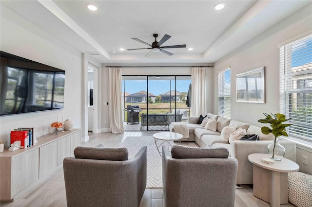 living room with light hardwood / wood-style flooring, a raised ceiling, and ceiling fan