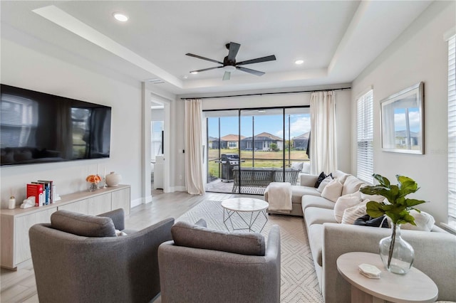 living room with light hardwood / wood-style flooring, ceiling fan, and a tray ceiling