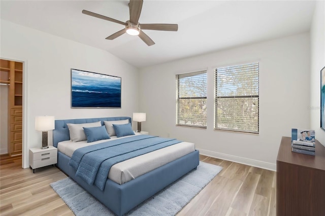 bedroom with ceiling fan, lofted ceiling, light hardwood / wood-style floors, and a walk in closet