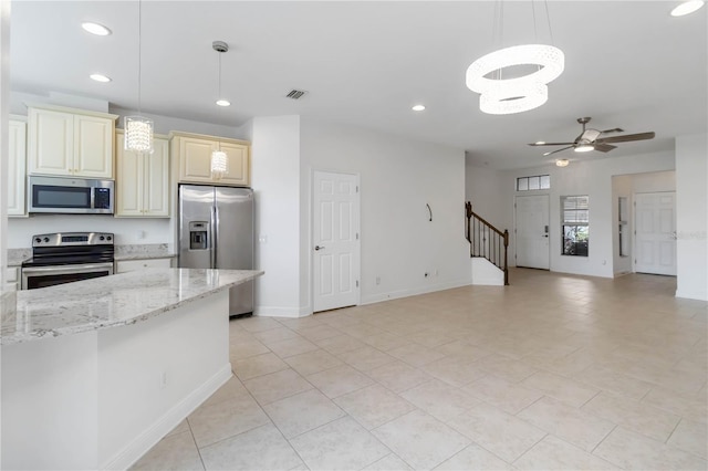 kitchen with pendant lighting, light tile patterned floors, stainless steel appliances, light stone counters, and cream cabinetry