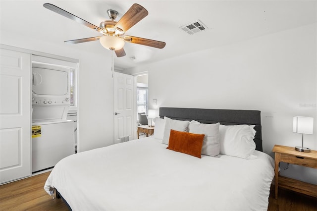 bedroom featuring stacked washing maching and dryer, hardwood / wood-style floors, and ceiling fan