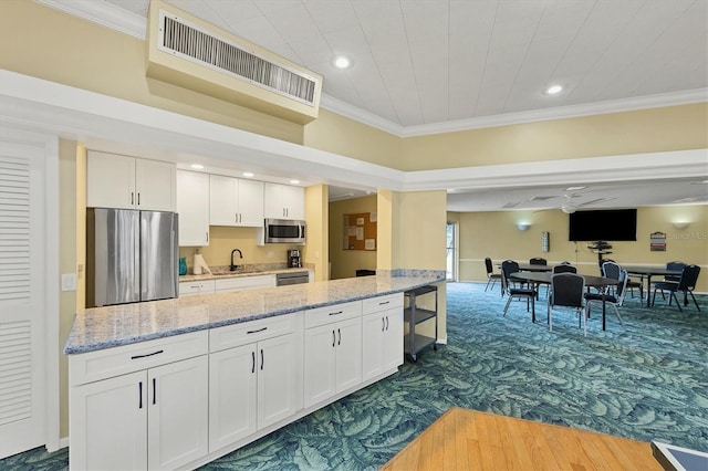 kitchen with crown molding, light stone counters, dark carpet, stainless steel appliances, and white cabinets