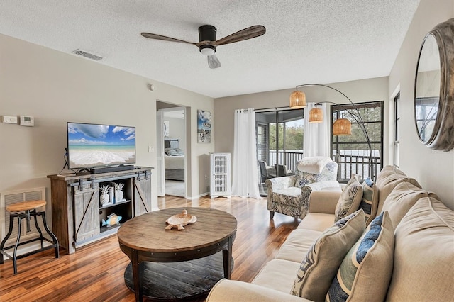 living room with hardwood / wood-style floors, a textured ceiling, and ceiling fan