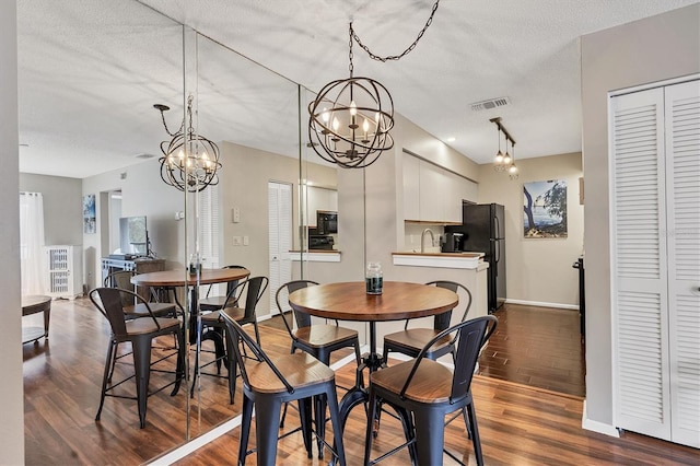 dining space featuring dark hardwood / wood-style flooring, a notable chandelier, sink, and a textured ceiling