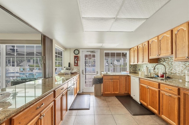 kitchen featuring dishwasher, light stone countertops, light tile patterned floors, and decorative backsplash