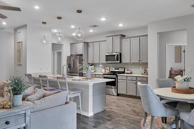 kitchen featuring gray cabinetry, tasteful backsplash, hanging light fixtures, appliances with stainless steel finishes, and hardwood / wood-style floors