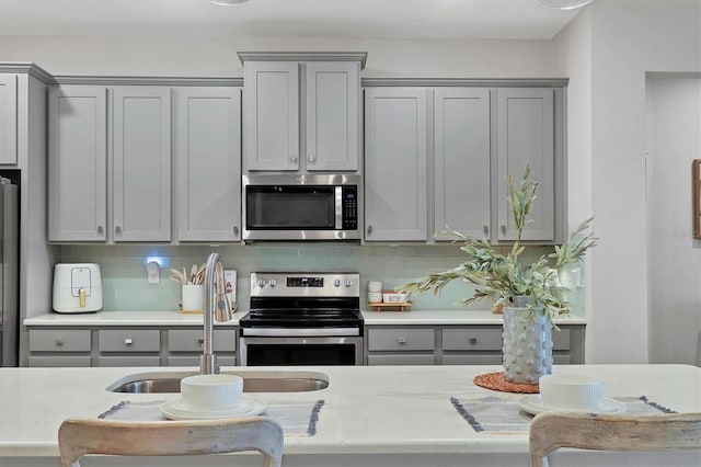 kitchen with backsplash, appliances with stainless steel finishes, sink, and gray cabinetry