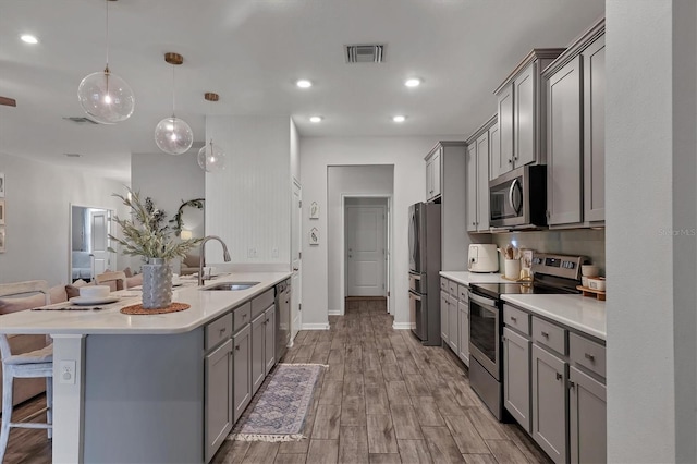 kitchen with sink, gray cabinetry, a kitchen breakfast bar, pendant lighting, and stainless steel appliances