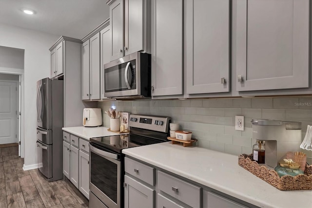 kitchen with stainless steel appliances, gray cabinetry, hardwood / wood-style floors, and decorative backsplash