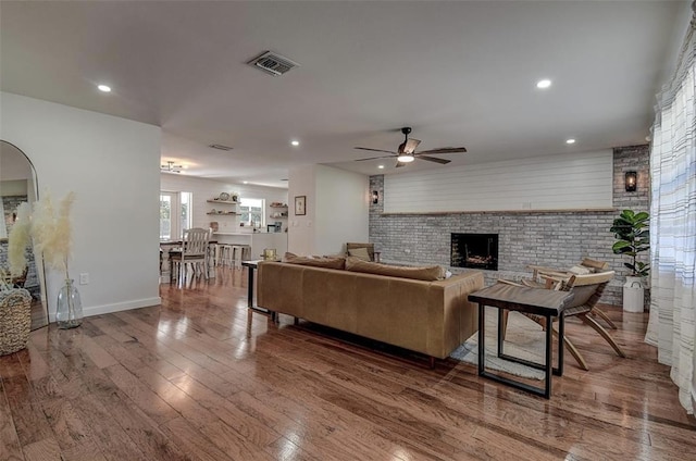 living room featuring a brick fireplace, wood-type flooring, and ceiling fan