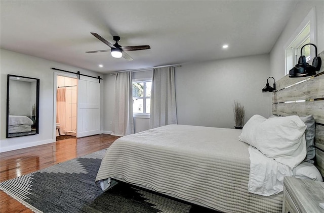 bedroom with ceiling fan, connected bathroom, a barn door, and hardwood / wood-style floors