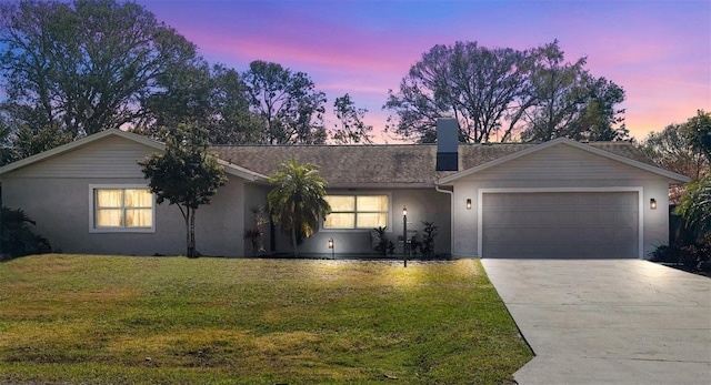 ranch-style house featuring driveway, a chimney, stucco siding, a garage, and a lawn