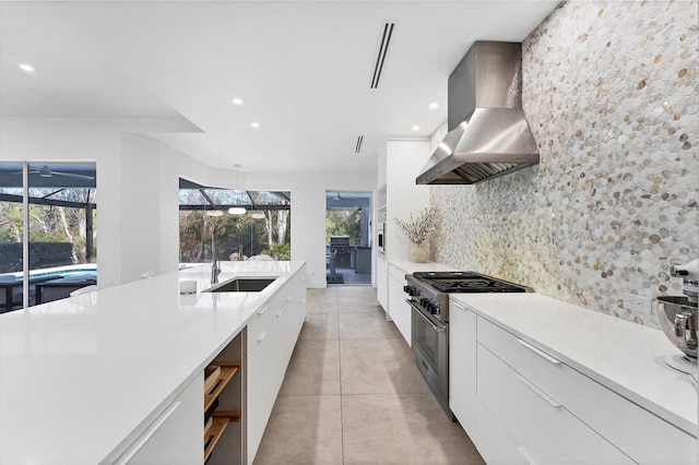 kitchen featuring high end stainless steel range oven, backsplash, a sink, modern cabinets, and wall chimney exhaust hood