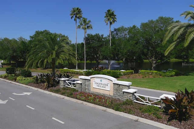 community / neighborhood sign featuring a water view and a lawn