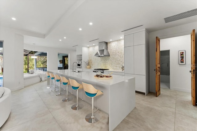 kitchen featuring a breakfast bar area, visible vents, decorative backsplash, wall chimney exhaust hood, and modern cabinets