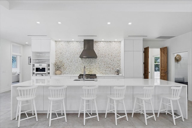 kitchen featuring wall chimney range hood, modern cabinets, white cabinetry, and decorative backsplash