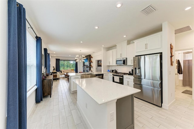 kitchen featuring decorative light fixtures, kitchen peninsula, a notable chandelier, stainless steel appliances, and white cabinets