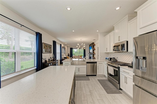 kitchen featuring white cabinetry, backsplash, decorative light fixtures, and appliances with stainless steel finishes