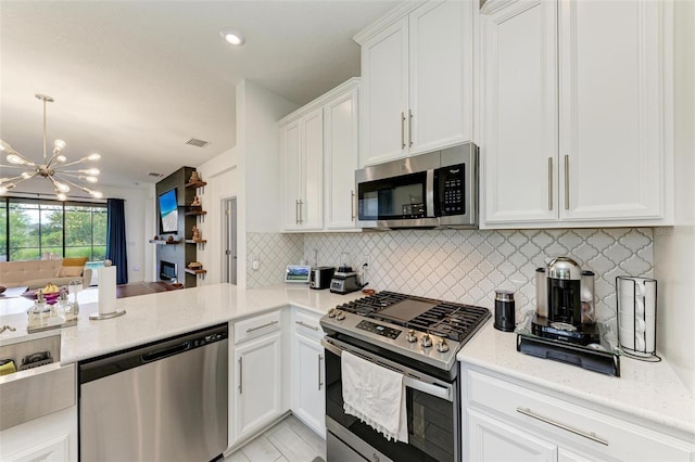 kitchen featuring white cabinetry, a chandelier, appliances with stainless steel finishes, light stone countertops, and decorative backsplash