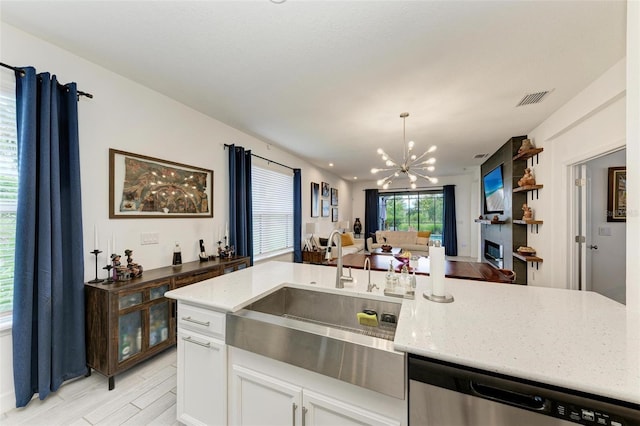 kitchen featuring sink, white cabinetry, an inviting chandelier, light stone counters, and stainless steel dishwasher