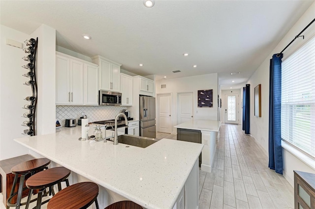 kitchen featuring stainless steel appliances, a kitchen bar, kitchen peninsula, and white cabinets