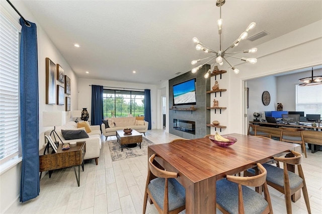 dining area with an inviting chandelier, a tiled fireplace, and light hardwood / wood-style flooring