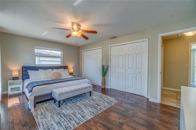 bedroom featuring two closets, dark wood-type flooring, and ceiling fan