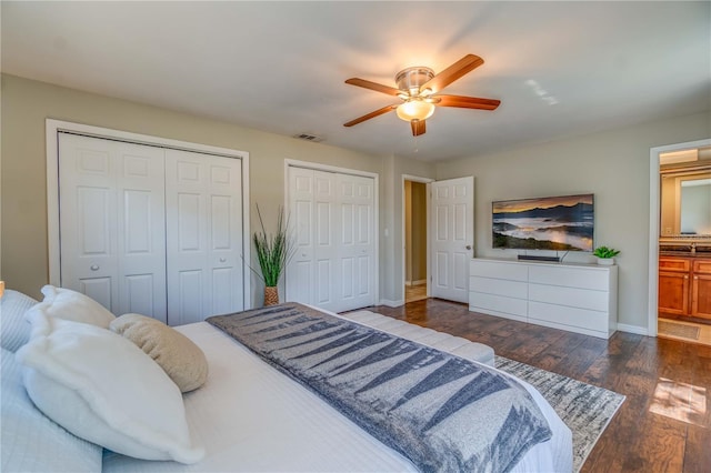 bedroom with dark hardwood / wood-style flooring, multiple closets, ensuite bath, and ceiling fan