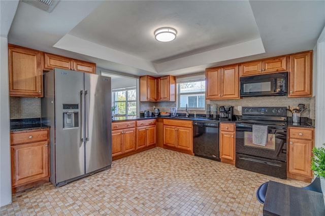 kitchen with sink, tasteful backsplash, dark stone countertops, a tray ceiling, and black appliances