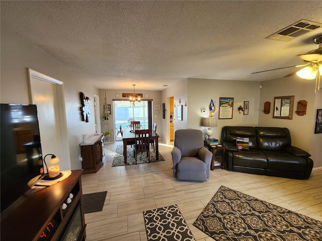 living room featuring ceiling fan with notable chandelier and a textured ceiling