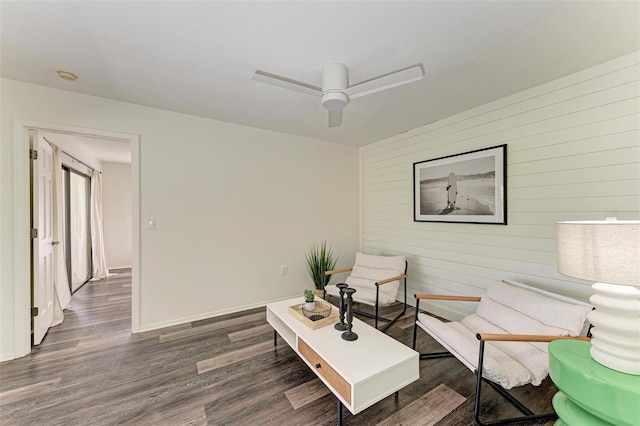 living room with dark wood-type flooring, ceiling fan, and wood walls