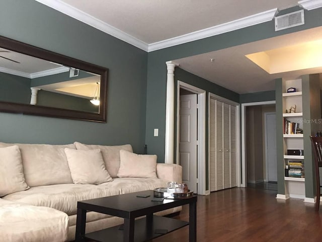 living room with dark wood-type flooring, crown molding, built in shelves, and decorative columns