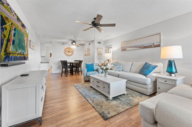 living room featuring ceiling fan, light hardwood / wood-style floors, and a textured ceiling