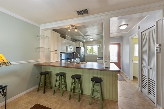 kitchen with a kitchen bar, crown molding, kitchen peninsula, decorative backsplash, and stainless steel fridge with ice dispenser