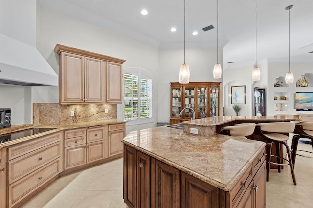 kitchen with sink, hanging light fixtures, an island with sink, black electric stovetop, and wall chimney range hood