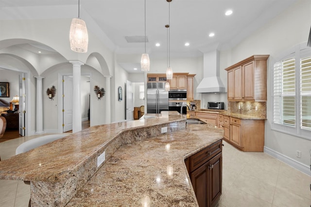 kitchen featuring decorative light fixtures, sink, a large island with sink, stainless steel appliances, and custom range hood