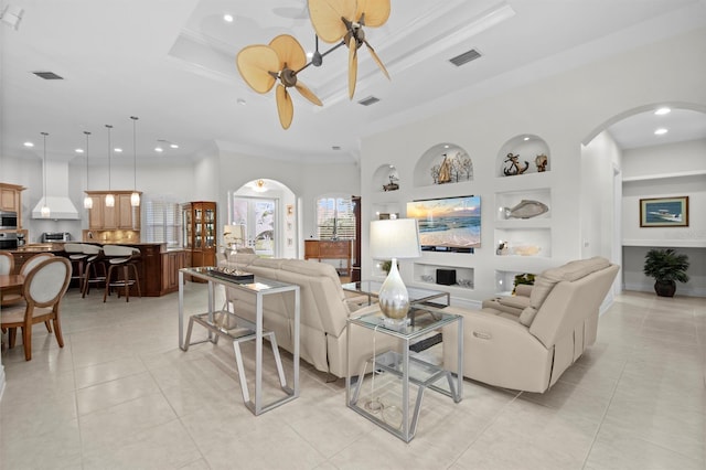 living room featuring a tray ceiling, built in shelves, and ornamental molding