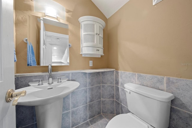 bathroom with sink, toilet, vaulted ceiling, and tile walls