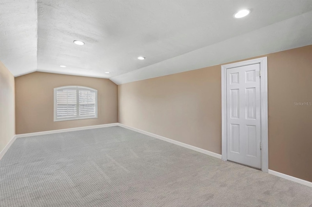 additional living space with vaulted ceiling, light carpet, and a textured ceiling