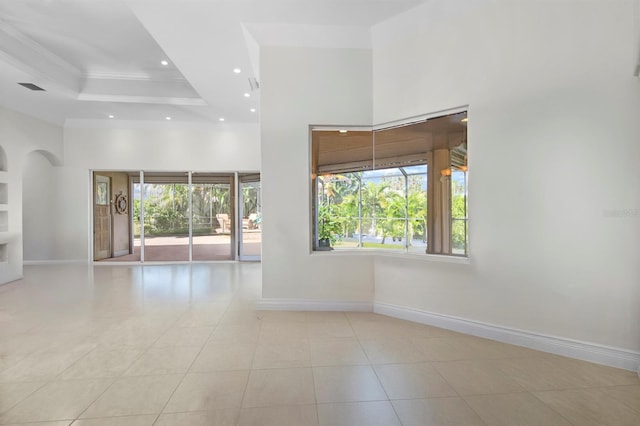 unfurnished room featuring a towering ceiling, ornamental molding, a raised ceiling, and a healthy amount of sunlight