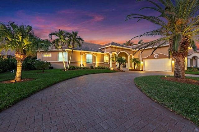 view of front facade featuring a garage, a yard, decorative driveway, and stucco siding